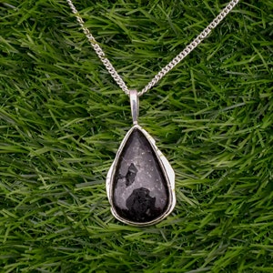 May include: A silver chain necklace with a teardrop-shaped pendant featuring a black gemstone.