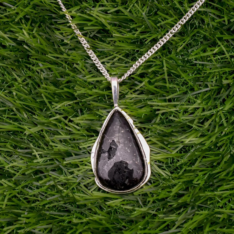 May include: A silver chain necklace with a teardrop-shaped pendant featuring a black gemstone.