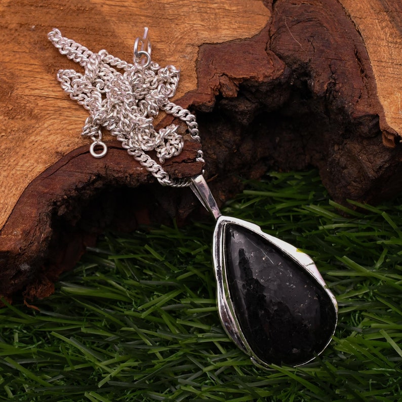 May include: A silver chain necklace with a black teardrop-shaped pendant. The pendant is set in a silver frame and has a smooth, polished finish.