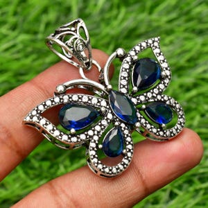 May include: Silver butterfly pendant with blue gemstone accents. The pendant has a detailed design with a filigree bail.