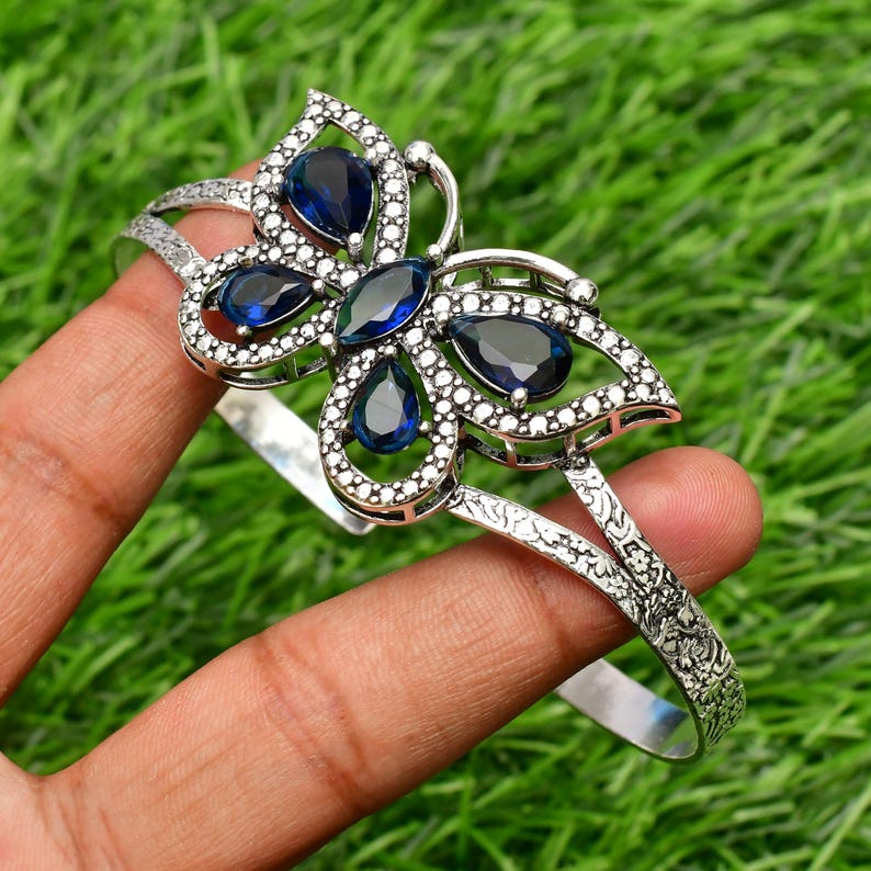 May include: A silver butterfly bangle bracelet with blue gemstone accents. The bracelet is open and has a delicate design.