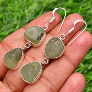May include: A pair of silver dangle earrings with two green gemstone drops on each earring.