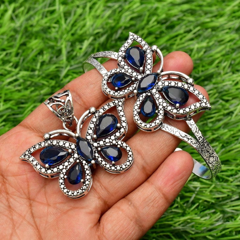 May include: A silver butterfly pendant and bracelet set with blue gemstone accents. The jewelry is made of silver and features a detailed butterfly design with blue gemstones.
