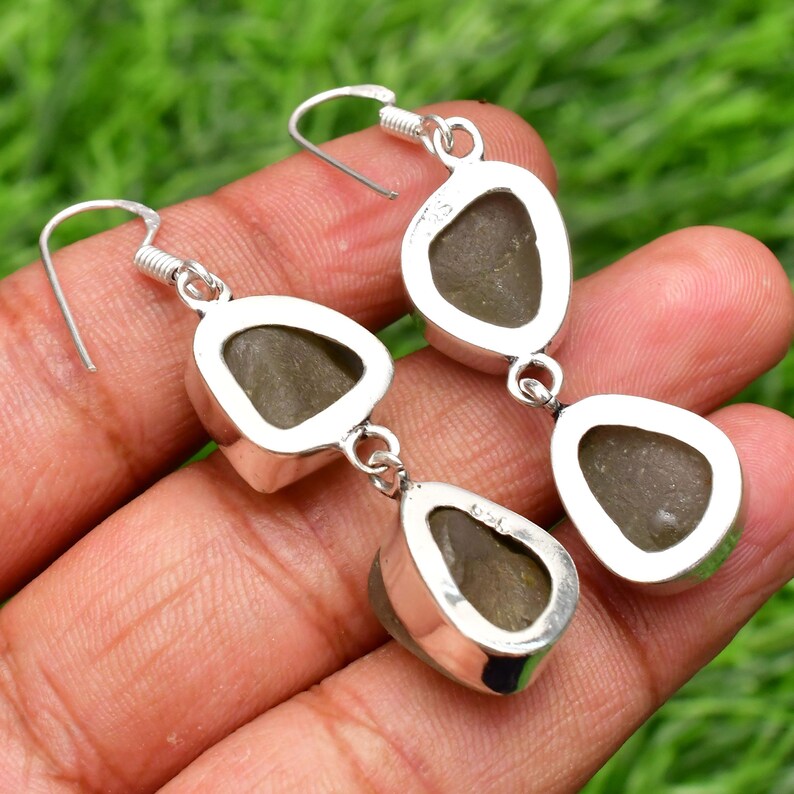 May include: A pair of silver dangle earrings with two teardrop-shaped green gemstones on each earring.