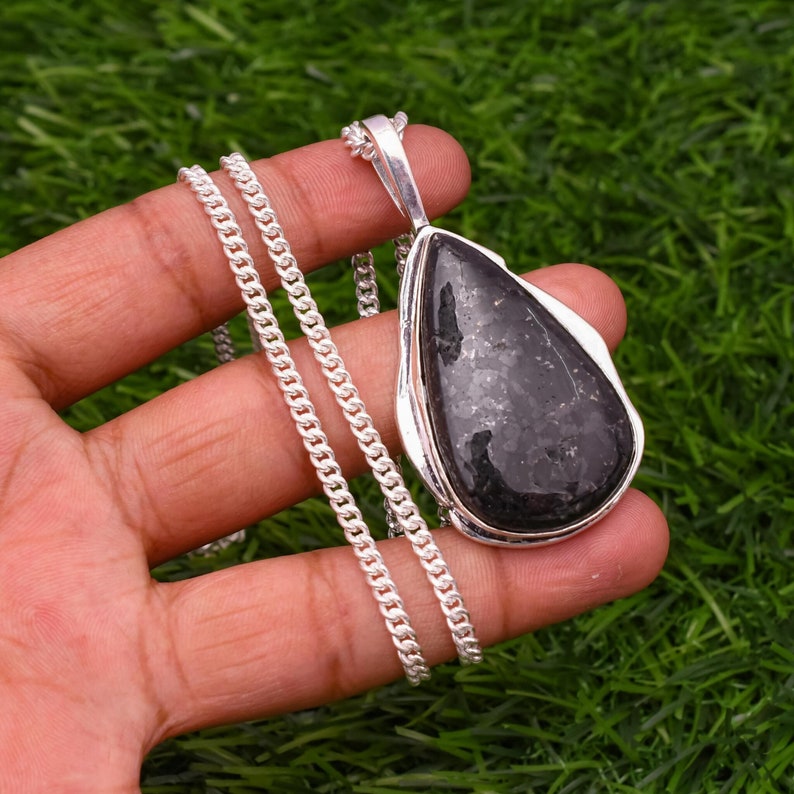 May include: A silver chain necklace with a black teardrop-shaped pendant. The pendant is made of a dark, sparkly stone.
