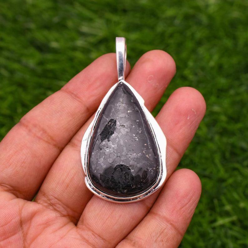 May include: A silver pendant with a black teardrop-shaped stone. The stone has a speckled, textured surface.