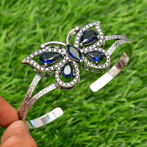 May include: Silver butterfly bangle bracelet with blue gemstone accents.
