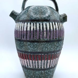 May include: A green ceramic pitcher with a speckled glaze and purple and red stripes. The pitcher has a wide mouth and a handle.