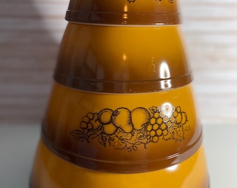 May include: Set of three brown and yellow mixing bowls with a grape and leaf design. The bowls are stacked on top of each other.