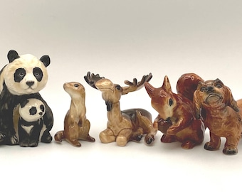 May include: A set of seven ceramic animal figurines, including a panda with a cub, a moose, a weasel, a squirrel, and a dachshund. The figurines are painted in realistic colors and have detailed features.