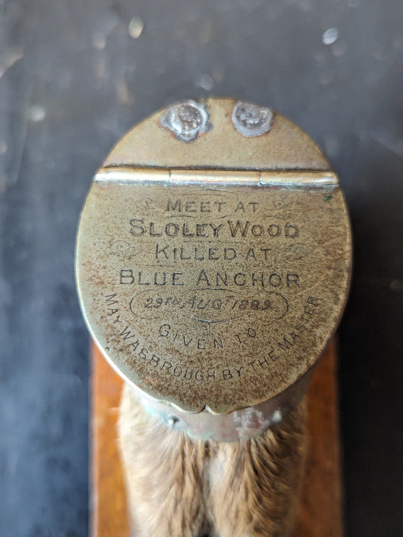May include: A brass bottle stopper with a round top and a fur-covered bottom. The top has an inscription that reads "MEET AT SLOLEY WOOD KILLED AT BLUE ANCHOR 29th JULY 1823 GIVEN TO WASBROUGH BY THE MASTER."