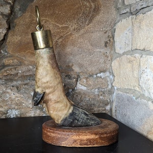 Op de afbeelding: Een vintage dierenpoot flessenstop met een messing dop en een houten voet. De poot is bruin en zwart met vacht.