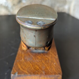May include: A vintage metal inkwell with a wooden base. The inkwell has a lid with the inscription "The Old Mill Ink Co.  Gloversville, N.Y."