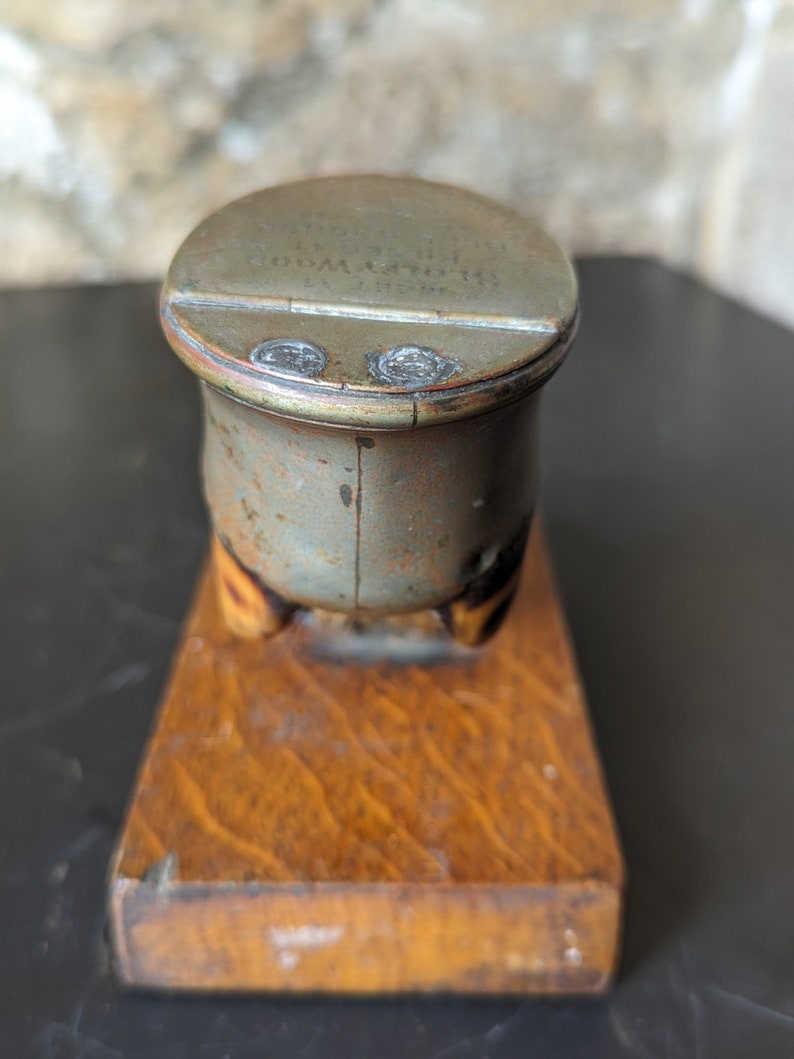 May include: A vintage metal inkwell with a wooden base. The inkwell has a lid with the inscription "The Old Mill Ink Co.  Gloversville, N.Y."
