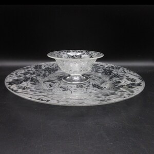 May include: A clear glass serving dish with a smaller bowl on top. Both pieces have a frosted design of leaves.
