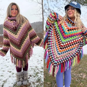 May include: Two handmade crochet ponchos. The first is a V-neck style in shades of purple, green, and beige with fringe. The second is a multi-colored, square-neck poncho with a variety of colors and fringe.