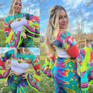 May include: A colorful crocheted crop top with bell sleeves. The top is made with a variety of bright colors, including pink, green, blue, and yellow. The sleeves are long and flowy, and the top is cropped at the waist.