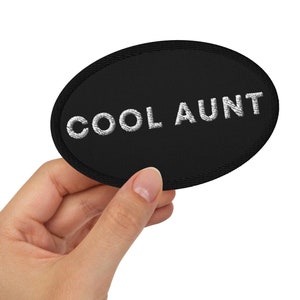 May include: Black oval patch with white embroidery that reads "COOL AUNT".