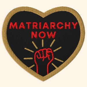 Può includere: Toppa ricamata a forma di cuore con sfondo nero e bordi dorati. Il testo rosso recita "MATRIARCHY NOW" sopra un pugno rosso con linee radianti.