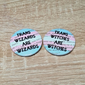 May include: Two round buttons with a transgender pride flag design. The text on the buttons reads "Trans Wizards Are Wizards" and "Trans Witches Are Witches".