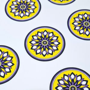 Op de afbeelding: Verschillende ronde stickers met een bloemenontwerp. Elke sticker heeft een gele kern, een paars en zwart bloemenpatroon en een paarse rand. De stickers staan op een witte achtergrond.