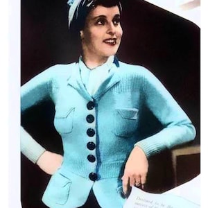 May include: A light blue knitted cardigan with a button-up front, two pockets, and a contrasting dark blue trim. The cardigan is worn by a woman with a light blue headscarf.