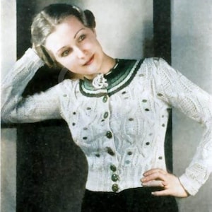 May include: A white long-sleeved knit cardigan featuring a textured cable pattern, a dark green ribbed collar, and a row of dark green buttons down the front. The garment has a fitted silhouette with ribbed cuffs and a ribbed hem at the waist.