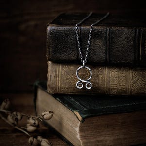 May include: A silver necklace with a circular pendant featuring a stylized double-loop design. The necklace is resting on top of a stack of antique books.