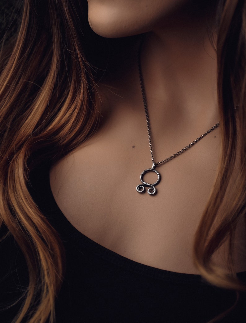 May include: A silver necklace with a unique pendant featuring a circle with two smaller circles attached to the bottom. The pendant is made of textured metal.