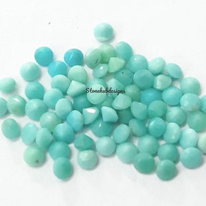 Puede incluir: Un montón de cabujones de piedra preciosa azul turquesa, cada uno con una forma redondeada ligeramente abovedada. Las piedras son lisas y pulidas, con un brillo sutil.