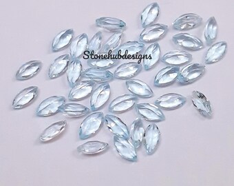May include: A collection of light blue marquise-cut gemstones scattered on a white surface. The gemstones are oval-shaped with pointed ends, and they have a translucent appearance. The text "Stonehubdesigns" is visible on the image.