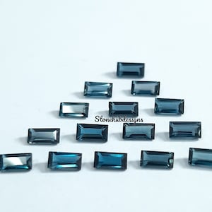May include: A collection of 15 blue rectangular gemstones, arranged in a triangular pattern on a white surface. The gemstones are faceted and have a dark blue color.