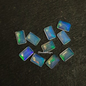 Könnte beinhalten: Eine Sammlung von zehn kleinen, rechteckigen, irisierenden Opal-Edelsteinen. Die Opale sind hellblau mit grün- und blauglänzenden Schimmern.