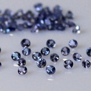 May include: A collection of small, round, blue gemstones. The gemstones are scattered on a white surface.