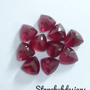 Puede incluir: Diez piedras preciosas rojas triangulares facetadas. Las piedras preciosas están dispuestas en un círculo sobre un fondo blanco.