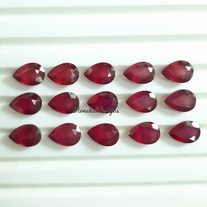 May include: A collection of 15 pear-shaped red gemstones, arranged in three rows of five. The gemstones are faceted and have a glossy finish.