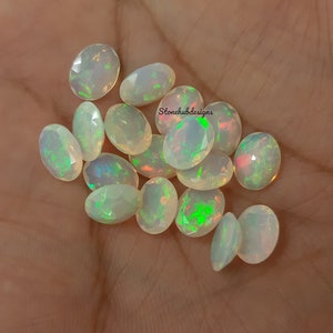 May include: A collection of oval-shaped, white opal gemstones with iridescent green and pink flashes. The stones are faceted and have a smooth, polished finish.