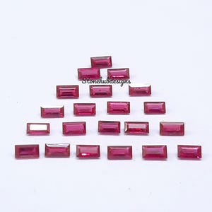 May include: A collection of 20 small, rectangular, pink gemstones. The gemstones are arranged in a triangular pattern on a white surface.