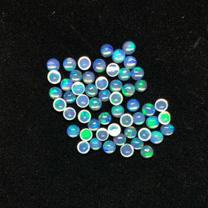 Puede incluir: Una colección de ópalos pequeños y redondos con una superficie pulida e iridiscente. Los ópalos muestran una gama de colores, incluyendo azul, verde y blanco, y están dispersos sobre un fondo negro. Estas piedras preciosas son ideales para la fabricación de joyas.