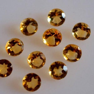 May include: Ten round, faceted, golden yellow gemstones. The gemstones are arranged in a scattered pattern on a white surface.