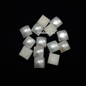 May include: A collection of white, square-shaped mother of pearl tiles. The tiles have a pearlescent sheen and are arranged in a random pattern.