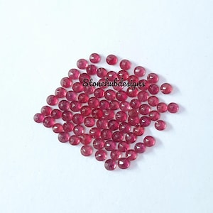 Op de afbeelding: Een stapel van ongeveer 50 kleine, ronde, rode edelstenen. De edelstenen zijn gefacetteerd en hebben een glanzende, gepolijste afwerking.