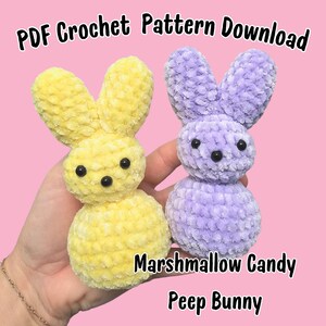 May include: Two crocheted marshmallow peep bunny amigurumi toys. One is yellow and the other is purple. The toys are held in a hand. The text "Marshmallow Candy Peep Bunny" is below the toys.