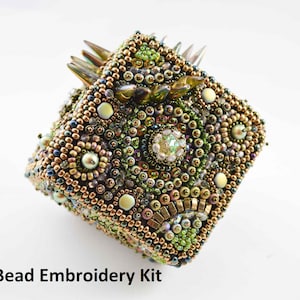 May include: A square bead embroidery kit with a complex design. The kit features a variety of beads in gold, green, and iridescent colors. The text "Bead Embroidery Kit" is at the bottom of the image.