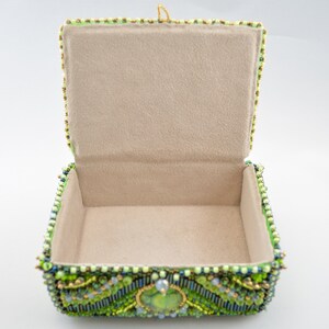 May include: A green beaded jewelry box with a light beige interior. The box is decorated with green, blue, and gold beads.