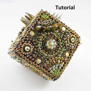 May include: A square-shaped beaded box with a green, gold, and brown color scheme. The box is covered in small beads and has a textured surface. The box has a pointed design on the top.