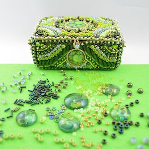May include: A green and gold beaded jewelry box with a decorative lid. The box is surrounded by green, gold, and silver beads.