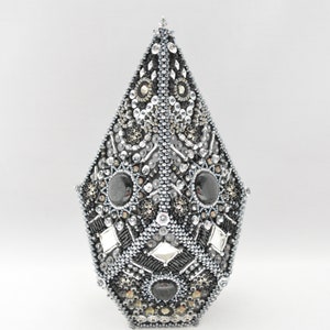 May include: A silver and black geometric ornament with a pointed top and a faceted design. The ornament is covered in beads, sequins, and small mirrors.