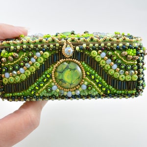 May include: A small green and gold beaded box with a green and gold marbled center piece. The box is decorated with various shades of green and gold beads.