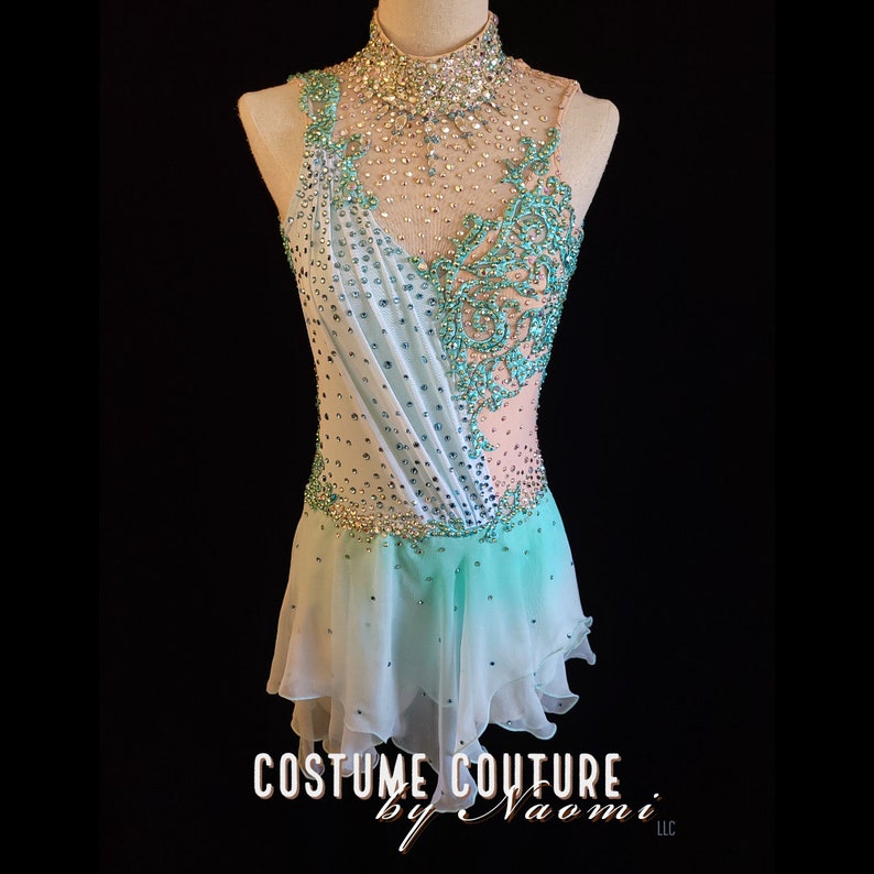May include: A light blue and white figure skating dress with a high neckline and a beaded design. The dress has a layered skirt and is embellished with rhinestones.